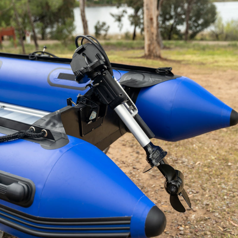 Bixpy motor assembly mounted on the stern of a blue inflatable boat, resting on land with trees in the background.