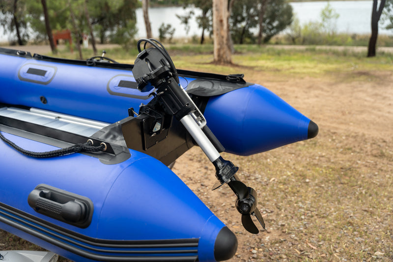 Bixpy electric outboard motor mounted on the stern of a blue inflatable dinghy, resting on land near water.