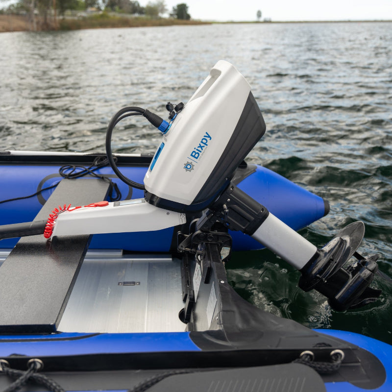 White Bixpy electric outboard motor with tiller handle mounted on a blue inflatable boat, propelling through rippled water.