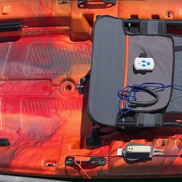 Close-up, top-down view of a white Bixpy remote control tethered on a grey kayak seat, with a Bixpy battery nearby on an orange and red camouflage kayak deck.