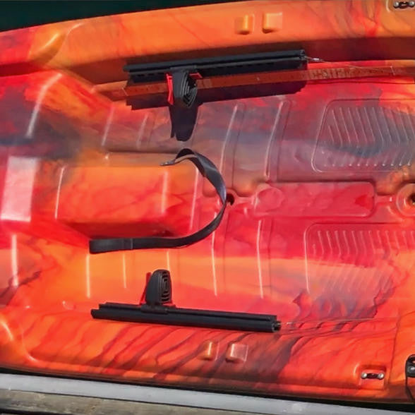 Close-up, top-down view of two black Foot Pedal Steering System tracks mounted on an orange and red camouflage kayak deck.