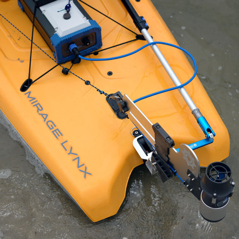 Top-down view of an orange Mirage Lynx kayak with a Bixpy Jet electric motor and battery system installed via a gray adapter, in shallow water.