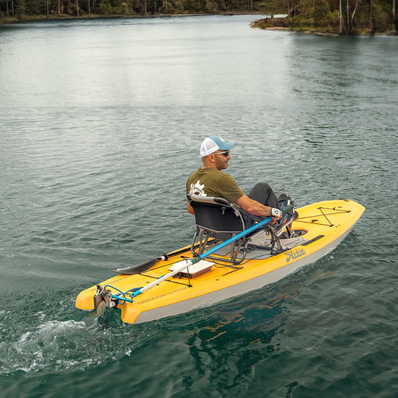 Man in a yellow Hobie pedal-drive kayak propelled by a Bixpy Jet electric motor, leaving a wake on calm water with a treed shoreline in the background.