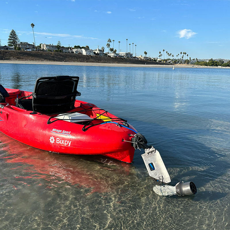 Red Mirage Sport kayak with a Bixpy Jet electric motor mounted and tilted up in shallow, clear water, showing its adaptation for pedal drive kayaks.
