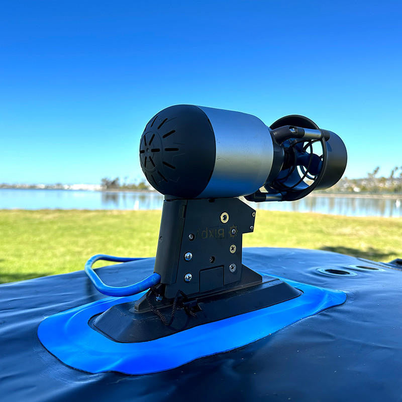 Low-angle view of a Bixpy Jet electric motor mounted on a black base with a blue adhesive patch, on a dark inflatable watercraft in an outdoor setting.