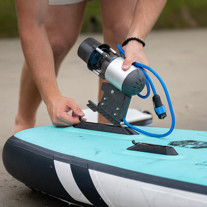 Person's hands inserting a Bixpy Jet electric motor and adapter into a light blue inflatable paddleboard.