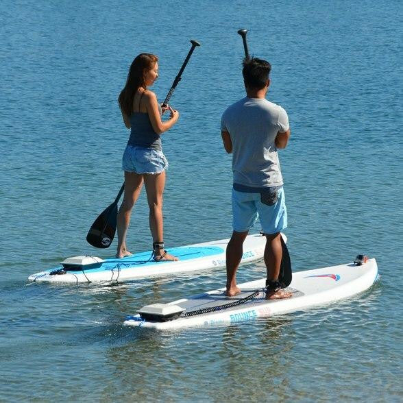 Two people paddleboarding on calm water using boards equipped with Bixpy motor adapters.