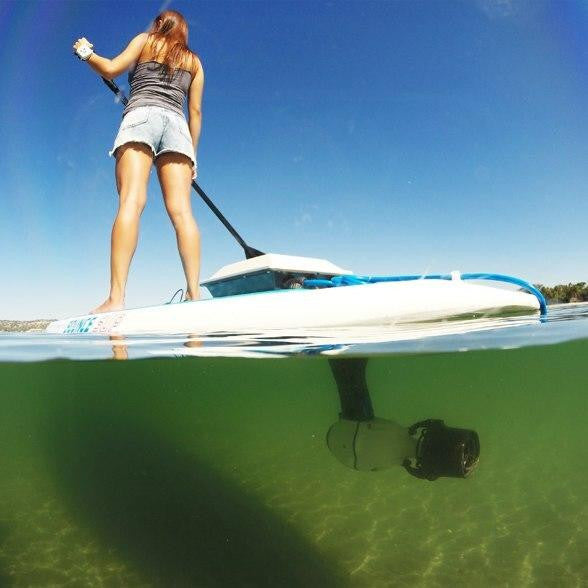 Low-angle split-shot of a woman paddling a stand-up paddleboard fitted with a Bixpy motor, showing both above and below the waterline.