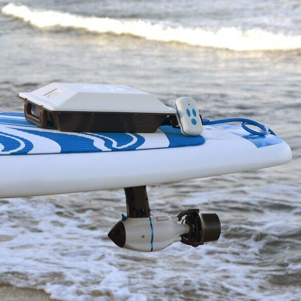 SUP paddleboard equipped with Slide & Lock Fin Adapter and J-1 motor, battery box, and remote, by the shoreline.