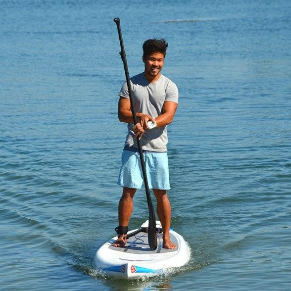 Man smiling while paddling on a stand-up paddleboard equipped with a Bixpy motor in calm coastal waters.