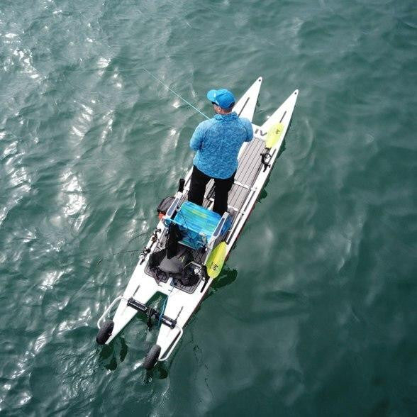 A man fishing on a catamaran-style paddleboard outfitted with gear and accessories, floating on calm ocean water.