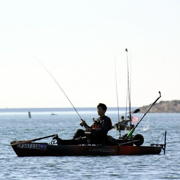 Man fishing from an orange and black Native kayak outfitted with a Bixpy Universal Kayak Adapter and motor, seated with multiple fishing rods on calm open water.