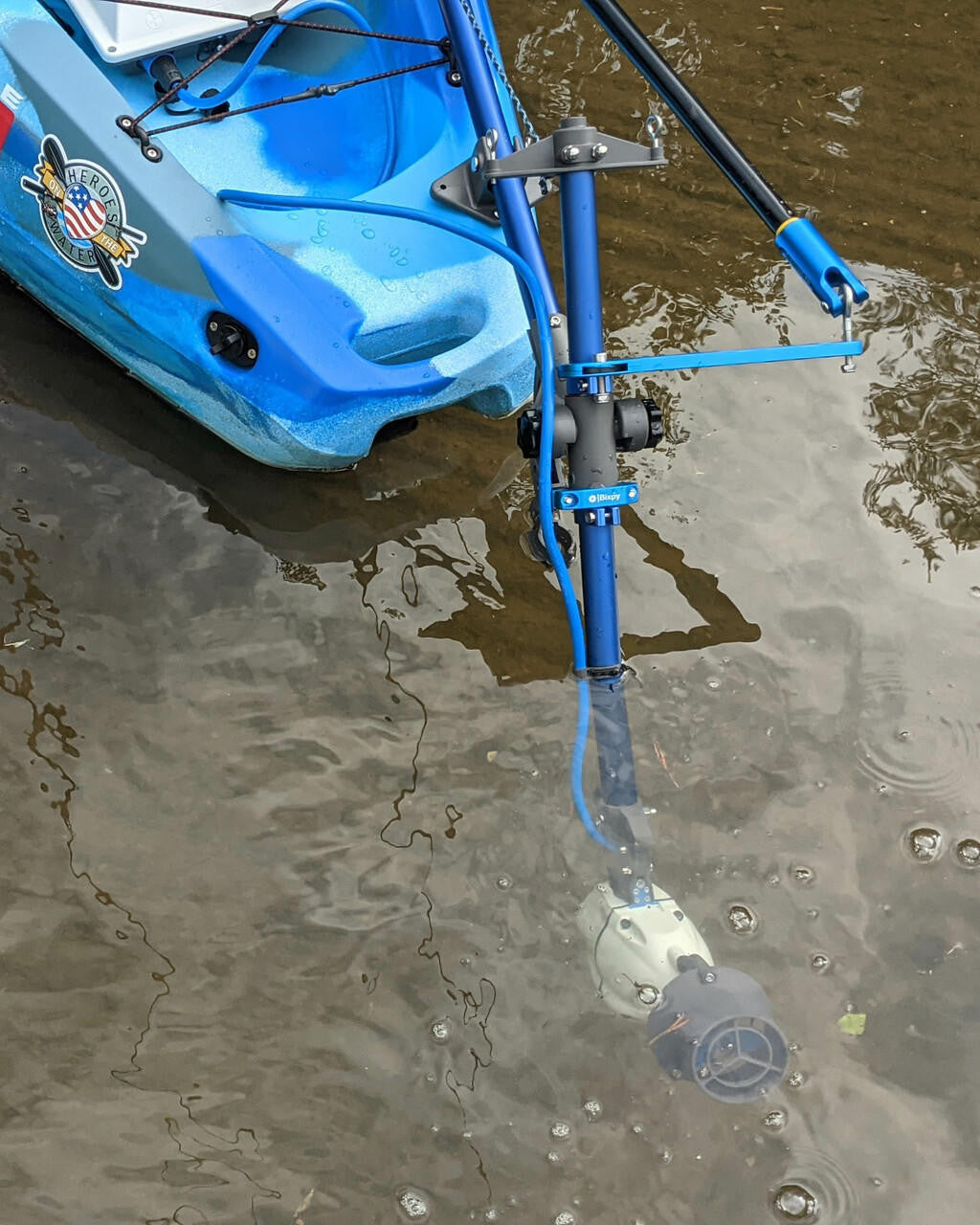 White Bixpy Jet electric motor submerged and extended from a blue kayak via a blue Universal Kayak Adapter in the water.