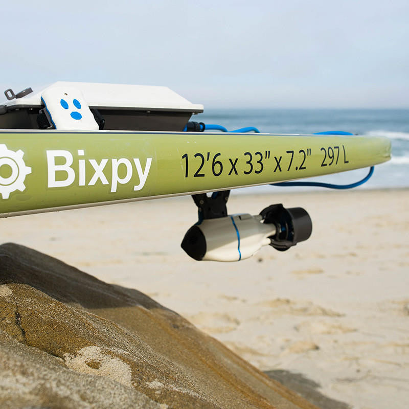Green Bixpy branded paddleboard with a Bixpy Jet electric motor mounted underneath, resting on a sandy beach.