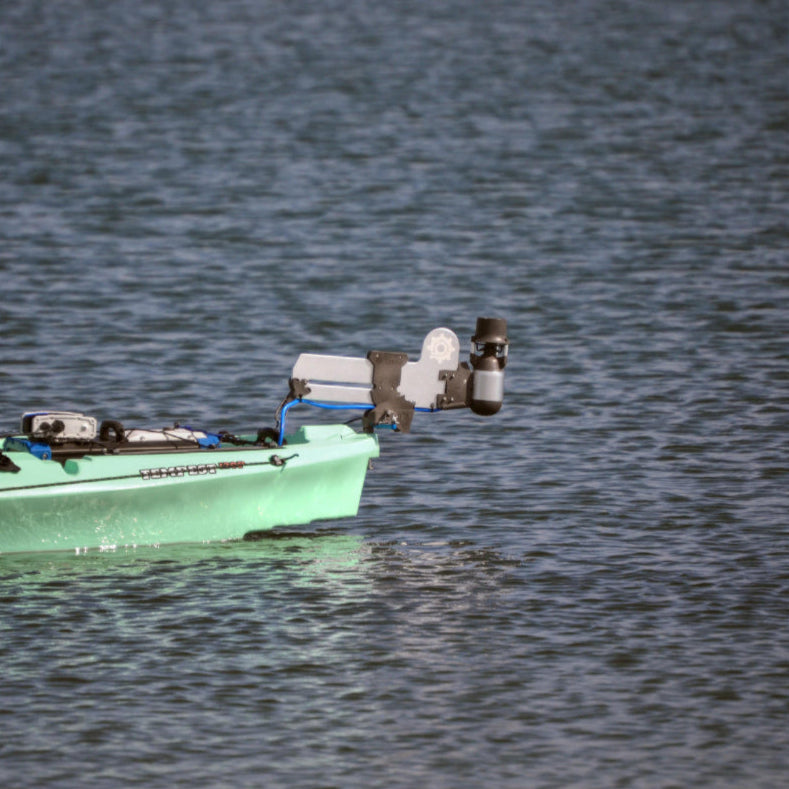Stern view of a light green kayak with a Bixpy Jet electric motor mounted on a rudder adapter, above rippled water.