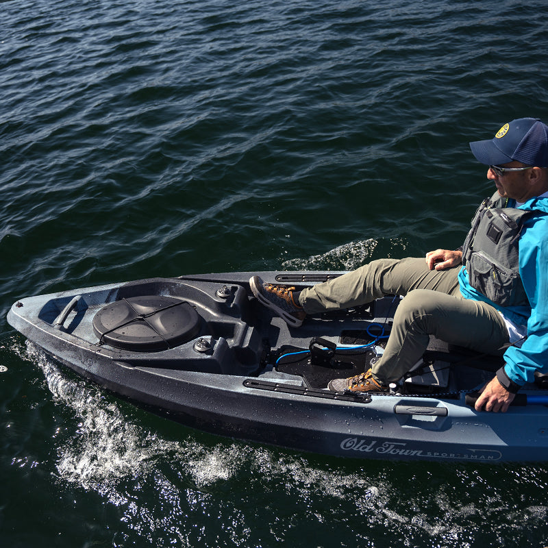Person in a grey Old Town Sportsman kayak, propelled by a Bixpy motor, moving across choppy water and leaving a wake.