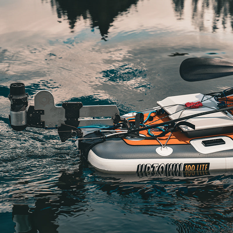 Bixpy Jet electric motor mounted to an inflatable gray and orange Uptown 100 Lite kayak via an integrated rudder mount, in calm water.