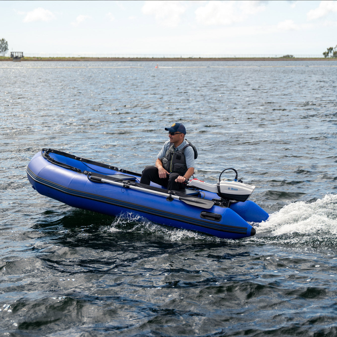 Man in a blue inflatable dinghy propelled by a Bixpy electric motor and battery pack mounted on the stern, moving across rippled water.