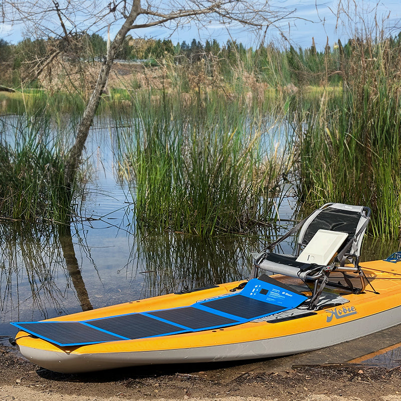 Bixpy Portable Solar Panel charging a battery pack on a Hobie kayak by a lake.