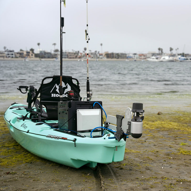 Light green Hoodoo Tempest kayak with a Bixpy motor and battery system on a beach with fishing rods and seaweed.